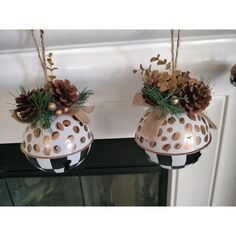 two white and gold decorated vases with pine cones on them hanging from a mantel