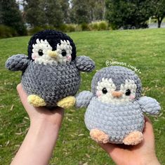 two small crocheted penguins are held up in the air by someone's hand