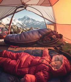 a sleeping bag on top of a bed in a tent with mountains in the background