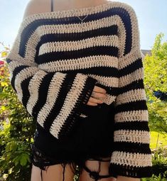 a woman wearing black and white crocheted sweater standing in front of some bushes