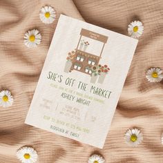 a white and green wedding card with daisies on the bed next to it is an image of a market booth