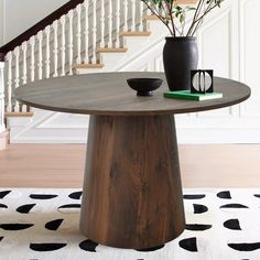 a wooden table sitting in the middle of a room next to a stair case and potted plant