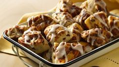 a pan filled with cinnamon rolls covered in icing on top of a yellow napkin