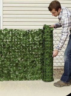 a man standing next to a fence made out of green plants and bushes with leaves on it