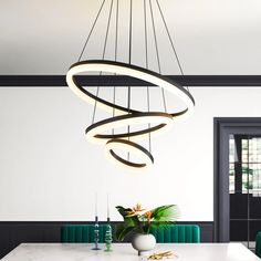 a modern chandelier hanging over a dining room table with green chairs and vases