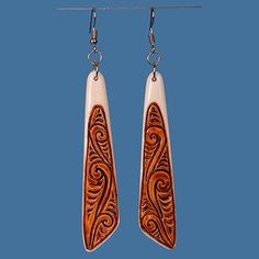 two long wooden earrings hanging from hooks on a blue background with an orange and white swirl design