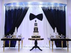 a table topped with a cake next to two black tables covered in white and gold decorations