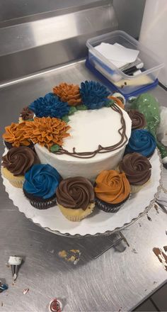 a white cake with blue, orange and brown frosting on it sitting on top of a metal counter