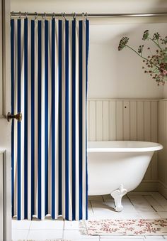 a bath tub sitting next to a shower curtain with blue and white stripes on it