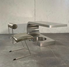 a modern desk and chair sitting on the floor in an empty room with concrete walls