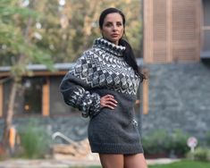 a woman standing in front of a house with her hands on her hips wearing a sweater