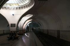 two people sitting on benches in a train station under a domed ceiling with lights above them