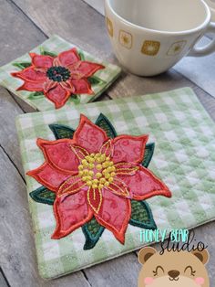 two coasters with poinsettia appliqued on them next to a coffee cup