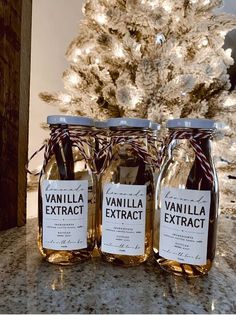 three jars filled with vanilla extract sitting on a counter top next to a christmas tree