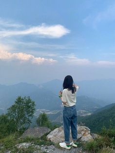 a woman standing on top of a mountain next to a lush green forest covered hillside