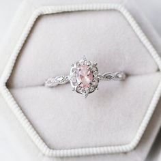 a pink diamond ring sitting on top of a white velvet cushioned box with beading around it