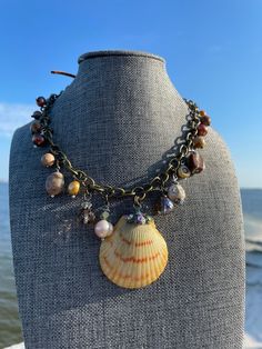 This necklace is truly one of a kind. The authentic organic shell is from the beaches of Northwest Florida. It has been left in it's natural state and adorned with petite rhinestones. The rhinestones have an aurora borealis luster that give it just the right amount of bling.  The finished shell pendant is attached to an antiqued bronze chain and beautiful sienna suede.  All along the necklace you will find freshwater pearls, whimsical beads, crystals, and  jasper gemstones that have been hand crafted into charms that dangle.  The necklace simply slips on and off over your head.  This is the perfect accessory for a beach wedding, coastal attire, boho and vintage clothing as well as a simple tee and jeans.  The length on the necklace is 15 inches each side (30 total in the neck area) from th Unique Shell-shaped Shell Necklaces, Unique Shell Necklaces, Unique Shell Pendant Necklace, Wire Wrapped Shell Necklaces In Shell Shape, Artisan Shell Jewelry For The Beach, Ocean-inspired Beaded Shell-shaped Necklace, Ocean-inspired Shell-shaped Beaded Necklaces, Wire Wrapped Shell Necklaces, Unique Abalone Shell Jewelry For Beach