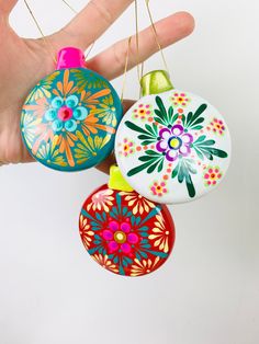 three colorful ornaments hanging from strings in someone's hand