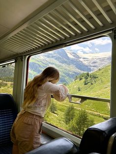 a woman looking out the window of a train with mountains in the backgroud