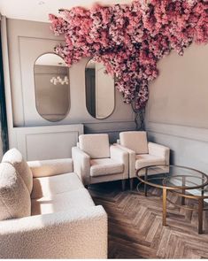 a living room filled with furniture and pink flowers on the wall above them is a mirror