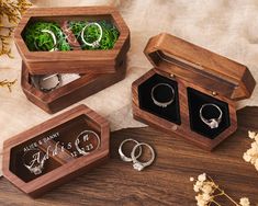 three wooden boxes with wedding rings inside on a table next to flowers and dried plants