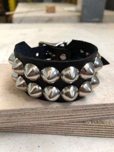 Classic studded punk bracelet with 2 rows of 1/2" cone studs. Fastens with a buckle and is adjustable. All hardware is nickle plated.Studs on black bracelets are nickel plated brass, studs on colored bracelets are nickel plated steel (old stock)Smaller bracelets have fewer studs per row.Made with hand dyed vegetable tan leather.Note: red bracelet is kind of pink-ish.Bracelet is 1.25" wide.Ask about custom sizing and color options! Punk Adjustable Cuff Bracelet With Rivets, Adjustable Punk Cuff Bracelet With Rivets, Punk Style Adjustable Cuff Bracelet With Rivets, Punk Black Bracelet With Silver Studs, Edgy Silver Studs Jewelry, Punk Leather Bracelet With Studs For Festivals, Silver Punk Bracelets With Spikes, Silver Punk Bracelets With Studs, Punk Style Silver Bracelet With Studs