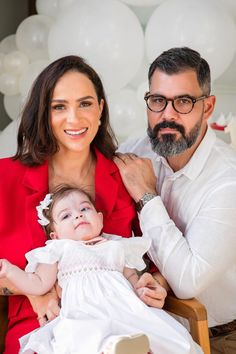 a man and woman holding a baby in front of white balloons on the wall behind them