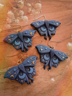 three blue butterfly shaped earrings sitting on top of a wooden table