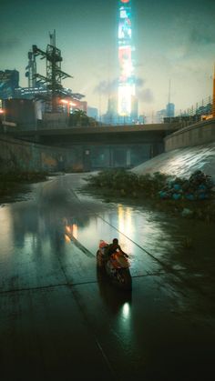 a man riding a motorcycle down a wet road next to a tall building at night