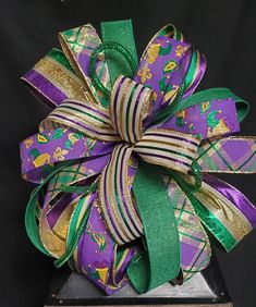 a purple and green bow on top of a wooden stand with ribbon around it's center