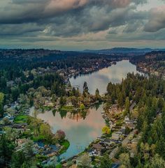 an aerial view of a lake surrounded by houses and trees with clouds in the sky