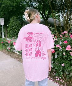 a girl in pink shirt standing on sidewalk next to flowers and trees with her back to the camera