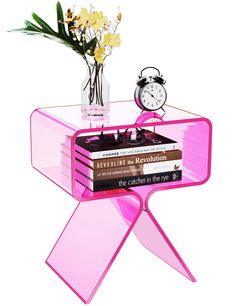 there is a pink table with books and a clock on it, next to a vase filled with flowers