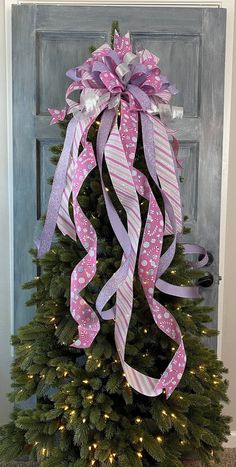 a decorated christmas tree in front of a door with pink and white ribbons on it