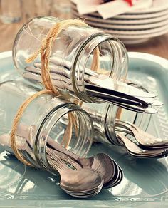 two glass jars with spoons and forks tied to each other on a blue plate