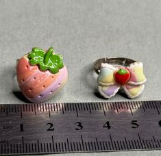 two rings sitting on top of a measuring tape next to a strawberry and a piece of fruit