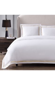 a bed with white sheets and gold trimmings on the headboard is shown