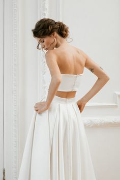 a woman in a white wedding dress looking down at her back with one hand on her hip