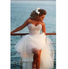 a woman in a short white dress leaning on a railing near the water with her legs crossed