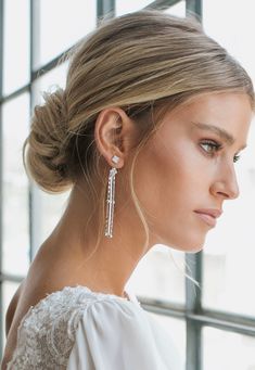 a woman with blonde hair wearing earrings and a white dress standing in front of a window