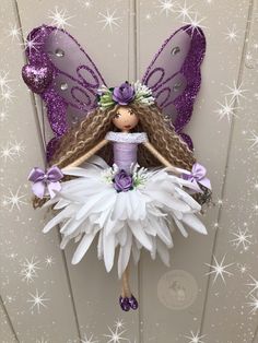 a purple and white fairy doll hanging from the side of a door with stars around it