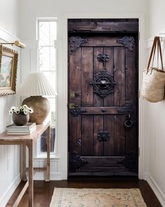 a large wooden door sitting inside of a room next to a table and lamp on top of a hard wood floor