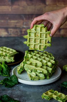 someone is holding up some green waffles on a plate with spinach leaves