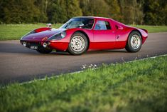 a red sports car driving down a road next to green grass and trees in the background