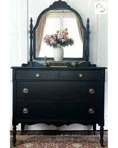 a black dresser with flowers on top and a mirror above it