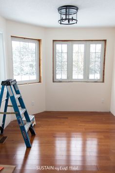 an empty room with hard wood flooring and ladder in the corner near two windows