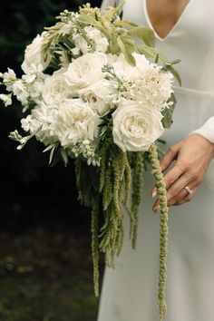 a woman holding a bouquet of white flowers in her hands and wearing a wedding dress