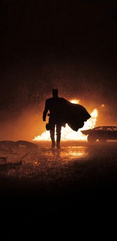 the silhouette of a man with a batman cape is walking in the rain at night