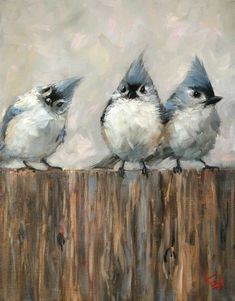 three little birds sitting on top of a wooden fence post in front of a gray sky