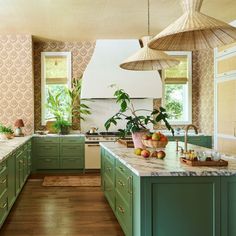 a large kitchen with green cabinets and marble counter tops, along with hanging lights above the island